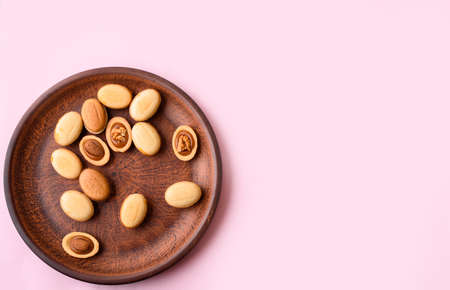 Homemade nuts with condensed milk, chocolate inside, walnuts and almonds. Dessert to tea on a plate on a light pink background. A place for text.の写真素材