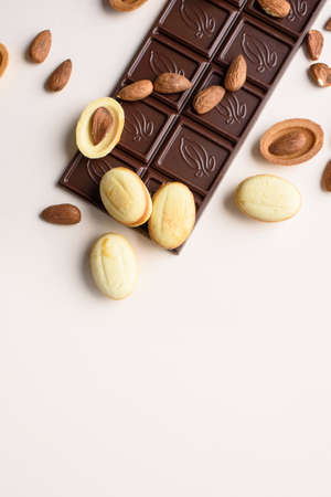 A bar of chocolate lies on a light background with almonds, walnuts, nuts with boiled condensed milk. View from above, place for text. Flat layの写真素材