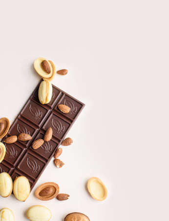 A bar of chocolate lies on a light background with almonds, walnuts, nuts with boiled condensed milk. View from above, place for text. Flat layの写真素材