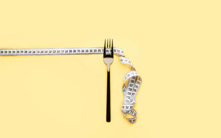 The fork lies on a colored background enquired by an inch. Proper nutrition, diet, place for text, view from above. Flat layの写真素材