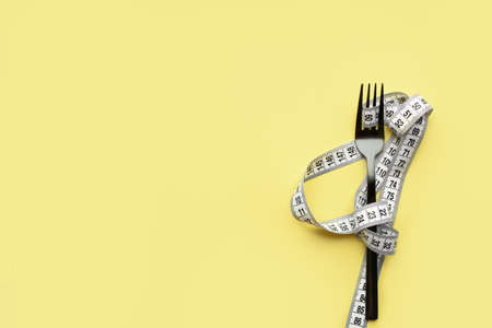 The fork lies on a colored background enquired by an inch. Proper nutrition, diet, place for text, view from above. Flat layの写真素材