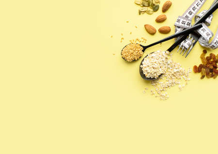 Two spoons of different sizes are filled with oatmeal and golden flax, raisins, almonds, pumpkin seeds. Healthy breakfast, proper nutrition, diet. A place for text.の写真素材