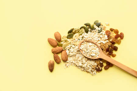 Two spoons of different sizes are filled with oatmeal and golden flax, raisins, almonds, pumpkin seeds. Healthy breakfast, proper nutrition, diet. A place for text.の写真素材