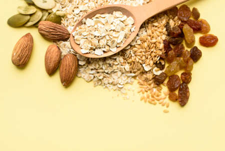 Two spoons of different sizes are filled with oatmeal and golden flax, raisins, almonds, pumpkin seeds. Healthy breakfast, proper nutrition, diet. A place for text.の写真素材