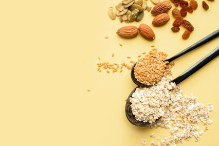 Two spoons of different sizes are filled with oatmeal and golden flax, raisins, almonds, pumpkin seeds. Healthy breakfast, proper nutrition, diet. A place for text.の写真素材