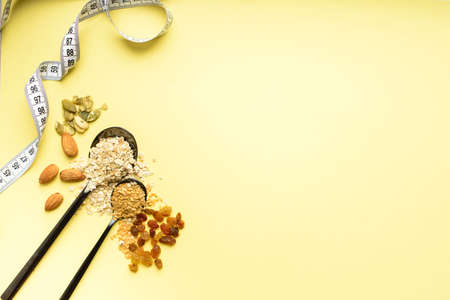 Two spoons of different sizes are filled with oatmeal and golden flax, raisins, almonds, pumpkin...