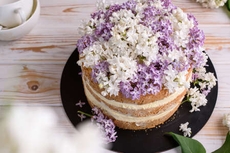 Biscuit cake with cream, impregnated with coconut and pineapple, decorated with lilac flowers. Delicious dessert, food photo.の写真素材