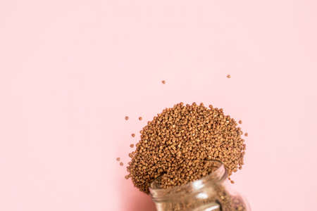 The buckwheat in a glass jar is scattered on a pink background.の写真素材
