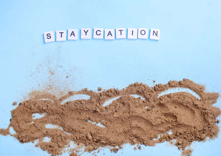 Beach sand on a blue background with wood letters and a word staycation. Holiday at home