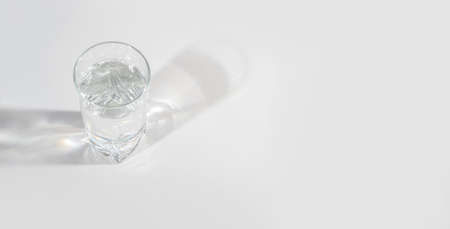 Glass glass with clean water on a light background with hard light and reflection. A place for text.の写真素材