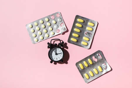 Plates with yolk pills and clocks on a pink background, hard shadows. Health. View from above, place for textの写真素材