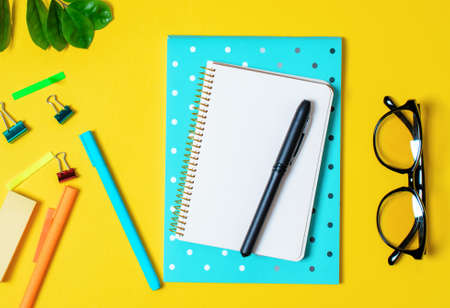 Yellow background, white notebook for records, phone, computer glasses, twig plants, pens pencils....