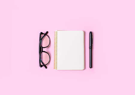 Notebook with clean sheets for records, hand holds pen, office glasses on a pink background. Flat layの写真素材