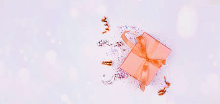 Banner of festive content. Festive box with ribbon, sequins, serpentine, side, on a light background. Flat layの写真素材