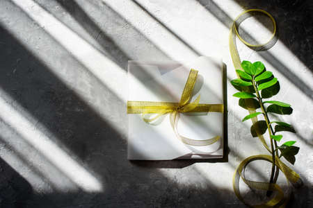 Packing a gift, in beautiful white paper, a golden ribbon. Hard shadows. Handmade packaging.の写真素材