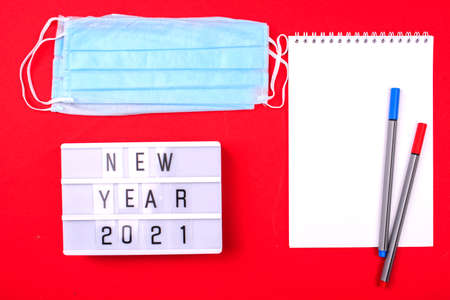 White notebook with pens, face mask, light box with the words New Year 2021. New year 2021 awareness. Coronavirus Pandemic Into 2021.の写真素材