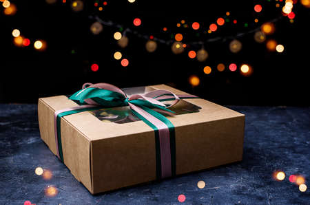 Box with satin ribbons and delicious treats for New Year and Christmas. New Years desserts on a dark...