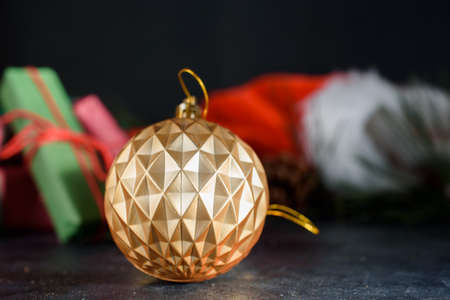 Beautiful golden color ball for decorating the Christmas tree, gifts, sprigs of spruce, santa hat in the background. New Years card for congratulations. New Years content.の写真素材