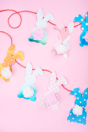 Easter bunny decoration paper cut background. DIY holiday handicraft garland of colorful rabbits and craft tools. Top view with copy space on pink background. Easter contentの写真素材