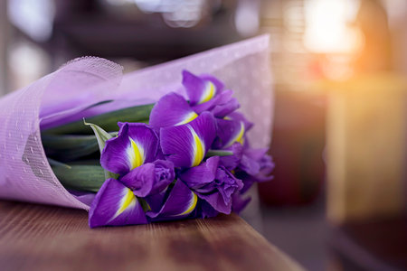 A beautiful and delicate bouquet of irises flowers in an interesting package lie on a wood table in a cafeteria. A place for text.の写真素材