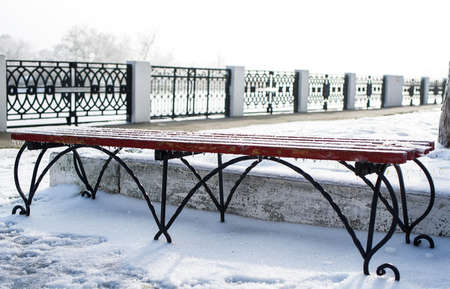 A walk through the winter city, a blue bench on the embankment is covered with snow and ice. Life...