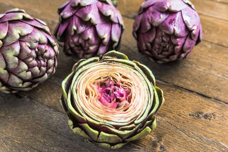 Three large purple fresh artichoke and a half on wooden backgroundの写真素材