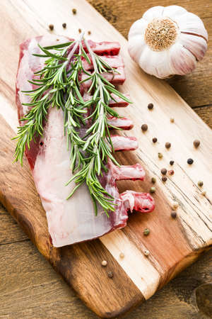 Raw lamb ribs with rosemary, pepper and garlic on wooden board.Top viewの写真素材