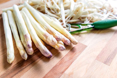 Peeled asparagus, ready for prepared, is on the wooden background. Peeler and peelings lie on the backgroundの写真素材