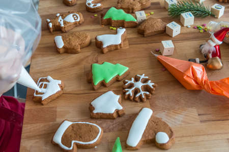 Women decorates christmas cookie in the shape of house. Some cookies are decorated. Wooden backgroundの写真素材