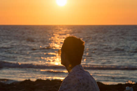 Young man looking at the sunset by the sea