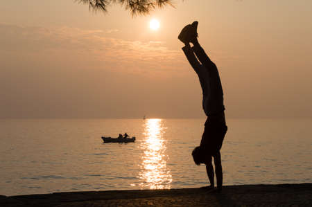Silhouette of a young man handstanding in front of the sea at susetの写真素材