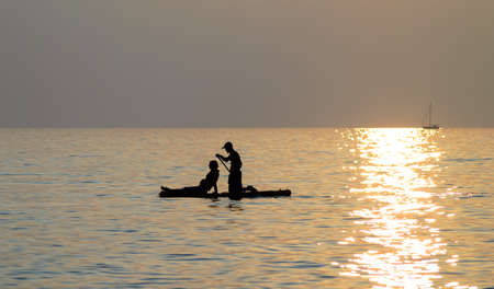 Young couple paddling in the ocean at sunset timeの写真素材
