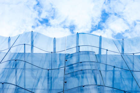 Detail of the wavy glass curtain wall facade of a nice modern building, sky and clouds reflecting on...