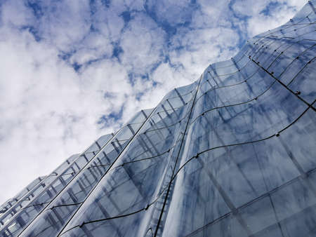 Detail of the wavy glass curtain wall facade of a nice modern building, sky and clouds reflecting on itのeditorial素材