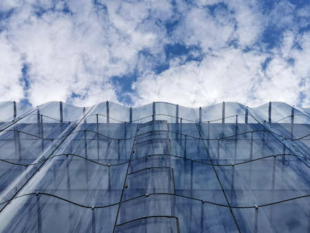 Detail of the wavy glass curtain wall facade of a nice modern building, sky and clouds reflecting on itのeditorial素材