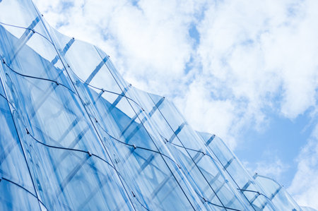 Detail of the wavy glass curtain wall facade of a nice modern building, sky and clouds reflecting on...
