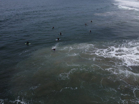 Aerial view of surfers catching waves near Manhattan Beach Pier under moody skiesâCalifornia's coast in motion from above.の写真素材