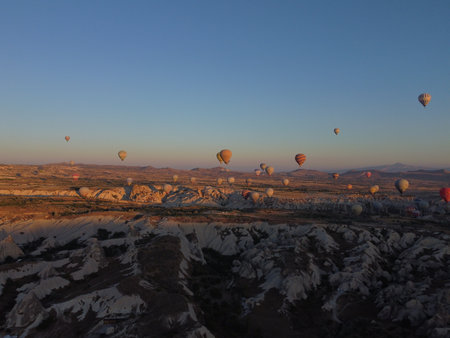 A magical drone shot of sunrise over GÃ¶reme as colorful hot air balloons lift off, painting the sky above the surreal Cappadocian landscape in golden light.の写真素材