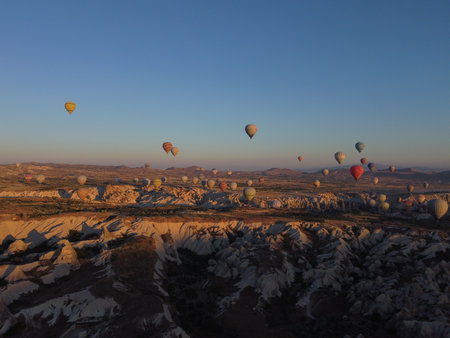 A magical drone shot of sunrise over GÃ¶reme as colorful hot air balloons lift off, painting the sky above the surreal Cappadocian landscape in golden light.の写真素材