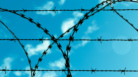 Barbed wire against blue sky and clouds.