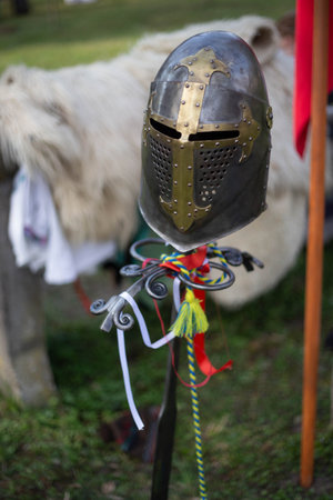 Medieval helmet is displayed on a metal stand adorned with colorful ribbons, evoking historical...