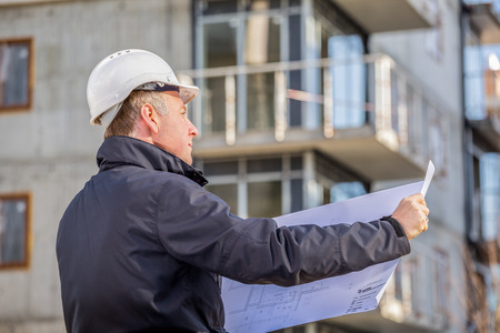 Construction manager with blueprints standing in front of construction site.の写真素材