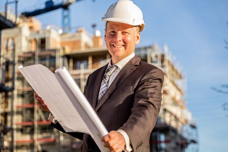 Construction manager with blueprints standing in front of construction site.の写真素材
