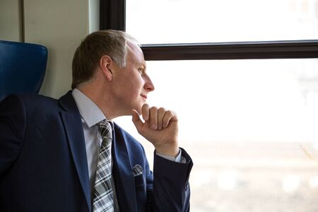Businessman interested in what he sees through window during his tripの写真素材