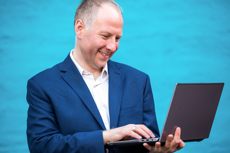 Young businessman with his laptop against turquoise wall