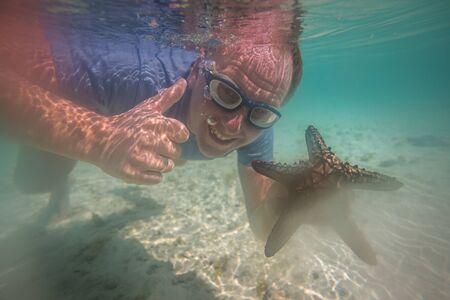 Happy tourist with starfish enjoying Indian ocean in Kenyaの写真素材
