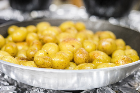 Many small potatoes fried on olive oil on silver frying panの写真素材