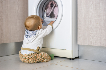 Baby boy interested in the cycles of washing machine doing laundryの写真素材