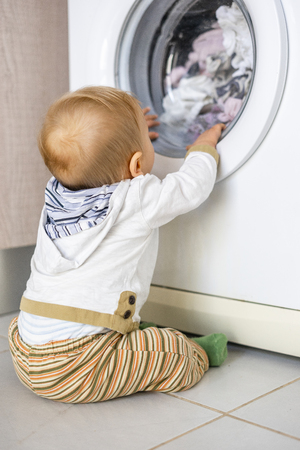 Baby boy interested in the cycles of washing machine doing laundryの写真素材