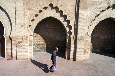 Marrakech, Morocco - January 7, 2020: Man with shopping walking along old mosque wall